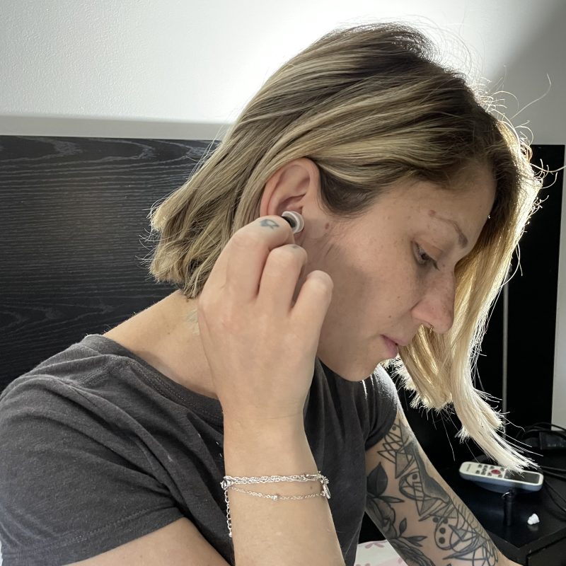 Person inserting BOLLSEN Earplugs Hearing Protection into her ear, wearing a grey t-shirt.