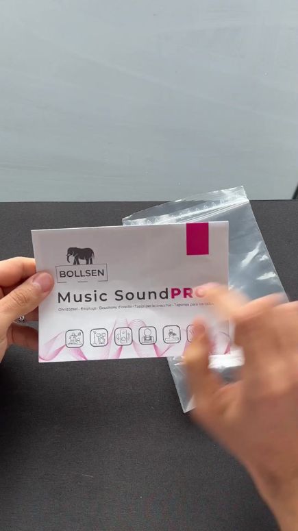 Hands holding a white instruction booklet with pink accents and a clear plastic bag.