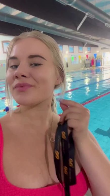 Young woman in a pink top holding black lanyards by a swimming pool.