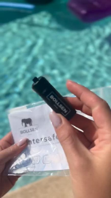 A person holds a black device and a white instruction sheet by a pool.